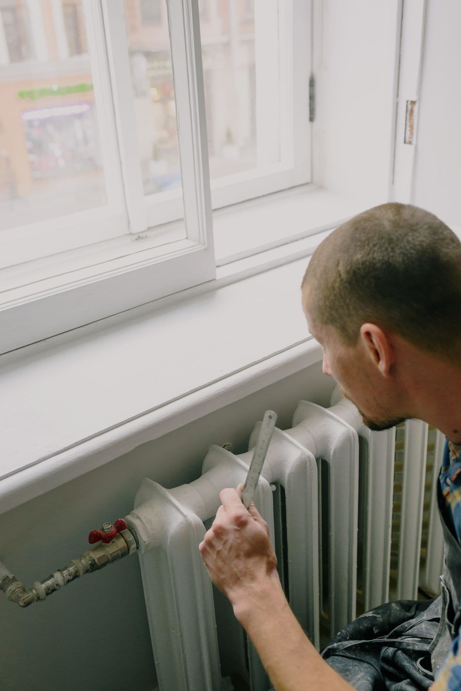 Stock technician measuring residential heating equipment below a window